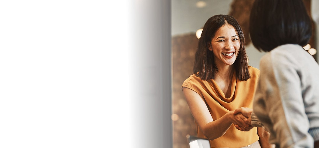 A woman smiling and shaking hands with a woman who’s back is to us