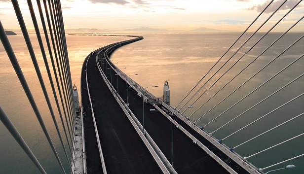 Looking down and outward toward a body of water from atop a suspension bridge at sunset