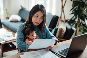 woman_with_laptop_reading_papers_holding_baby_300x200